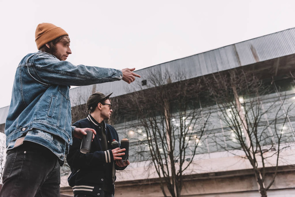 mužské pouliční umělci drží plechovky s sprejem a ukazoval na budování - Fotografie, Obrázek