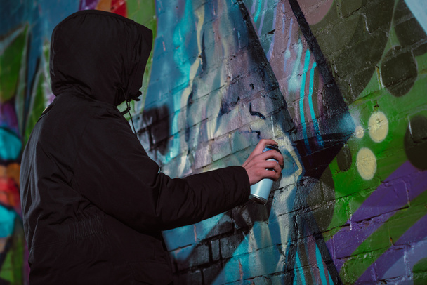 anonymous painting graffiti with aerosol paint on wall at night - Photo, image