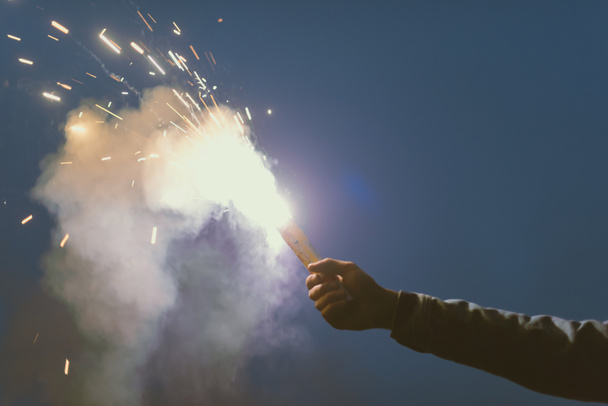 vista recortada de la mano masculina con bomba de humo con chispas en la noche
 - Foto, Imagen