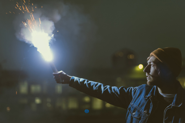 hombre holsing humo bomba con chispas en la noche
 - Foto, Imagen