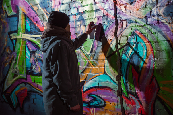 street artist painting graffiti with aerosol paint on wall at night - Φωτογραφία, εικόνα
