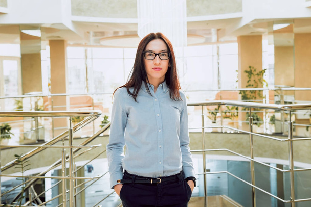 Confident brunette businesswoman in glasses in office hall - Фото, изображение