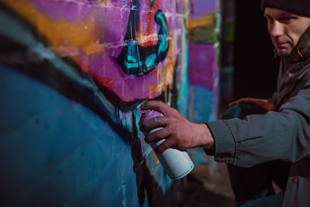 man painting graffiti with aerosol paint on wall at night - Photo, Image