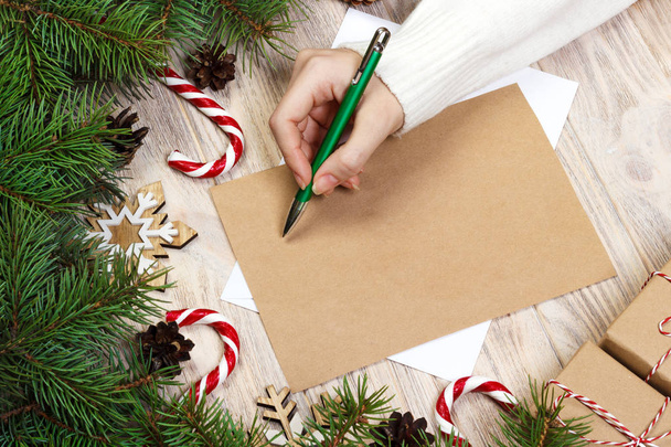 Female hands writing a letter to Santa Claus. Christmas gifts on a wooden background. View from above - Photo, Image