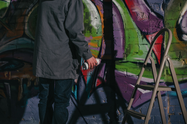 cropped view of street artist painting graffiti with aerosol paint on wall at night - Foto, afbeelding