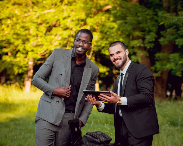 Two young multicultural businessmen at work in park. Concept of remote work. - Foto, Imagen