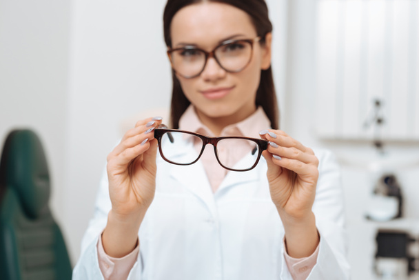 selective focus of ophthalmologist holding pair of eyeglasses in hands in clinic - Foto, Imagem