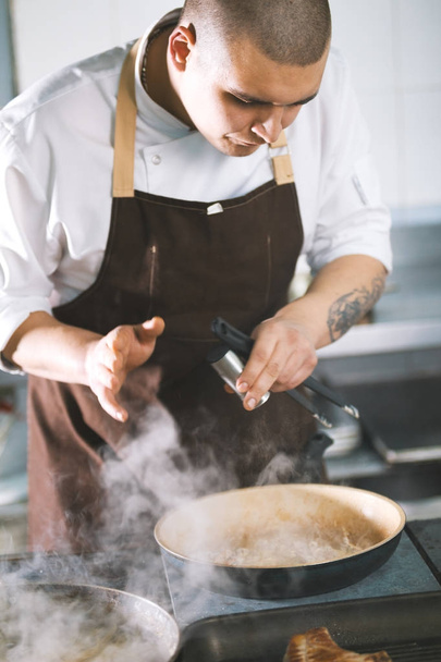 Jeune beau cuisinier masculin avec uniforme préparant une saucisse de viande
. - Photo, image