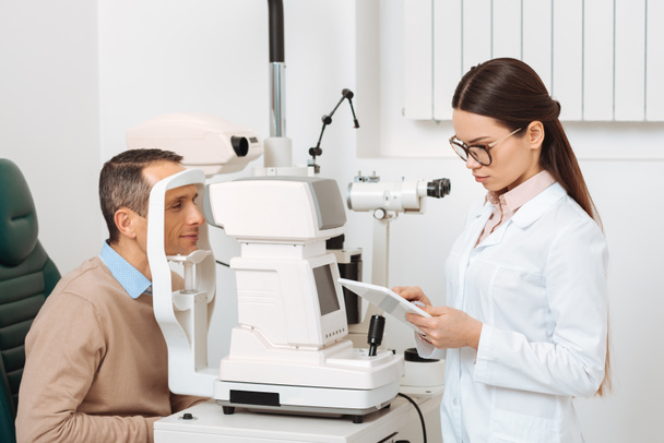 Widok z boku pacjenta coraz badania oczu w szczelinę lampa w klinice - Zdjęcie, obraz