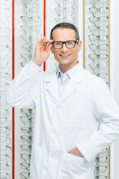 portrait of smiling oculist in eyeglasses standing in optics - Foto, Bild