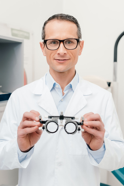 portrait of optometrist in white coat holding trial frame in hands in clinic - Foto, afbeelding