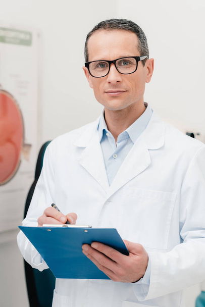 πορτρέτο του γιατρού με το σημειωματάριο στα χέρια βλέπουν τα φωτογραφικών μηχανών στην κλινική - Φωτογραφία, εικόνα