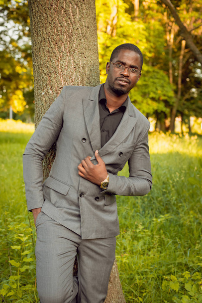 Young african man in grey suit at park near tree - Φωτογραφία, εικόνα