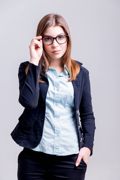 Young businesswoman with glasses in the office before gray wall - Foto, afbeelding