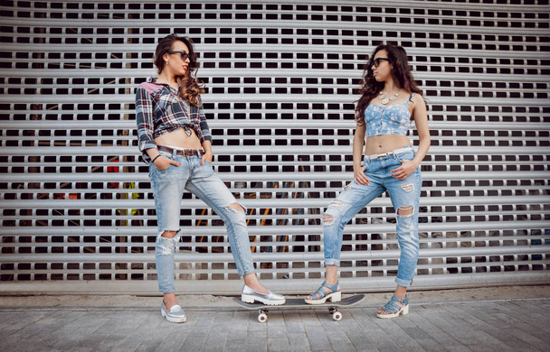 Two young mixed race girls in casual outfits walking with skateboard around streets - Foto, imagen