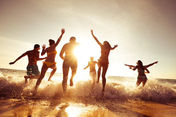 Big company of friends having fun at sunset beach - Foto, afbeelding