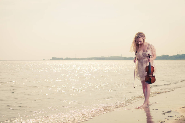 Woman on beach near sea holding violin - Fotoğraf, Görsel