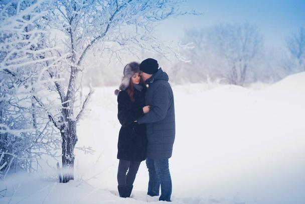 A loving couple on a winter walk. Snow love story, winter magic. Man and woman on the frosty street. The guy and the girl are resting on the snow. Christmas mood of a young family. - Zdjęcie, obraz