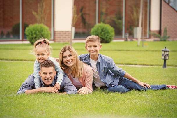 Happy family lying on green grass in courtyard near their house - Photo, Image