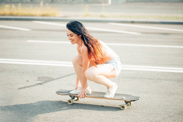 Beautiful young girl sits and ride on longboard in sunny weather - Foto, Imagem
