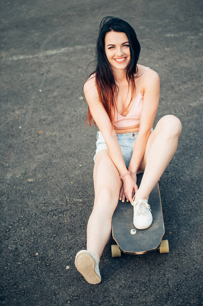 Beautiful young girl with tattoos sits on longboard in sunny weather - Фото, зображення