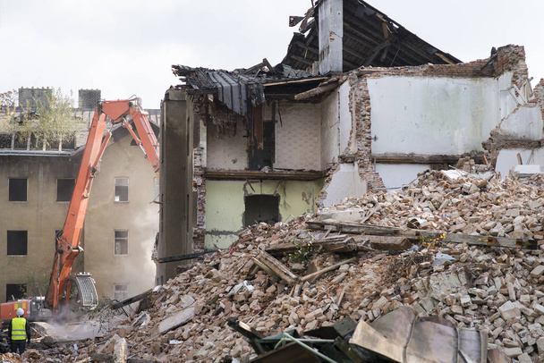 Mezza casa di mattoni crollata ricoperta di polvere e detriti con una macchina frantumatore
 - Foto, immagini