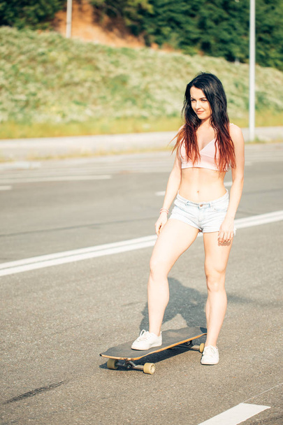 Beautiful sexy young girl in short shorts standing with longboard - Photo, image