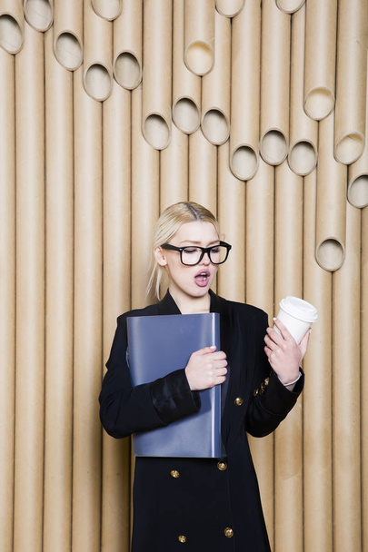 Красива здивована блондинка бізнес-леді в чорній сукні і окулярах з чашкою кави
. - Фото, зображення