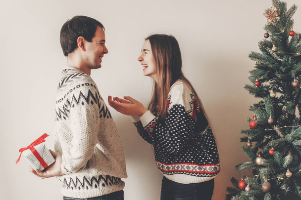 jovem feliz dando presente a sua mulher perto da árvore de Natal
  - Foto, Imagem