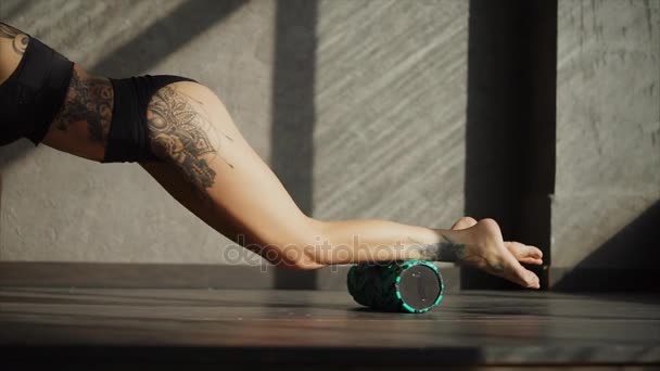 Strong girl is rolling fitness cylinder on her anterior surface of shins - Felvétel, videó