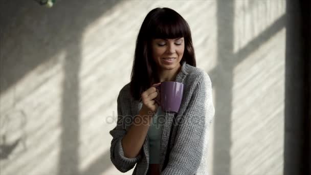 a beautiful lady sits by the window and drinks a hot drink from a glass - Video, Çekim