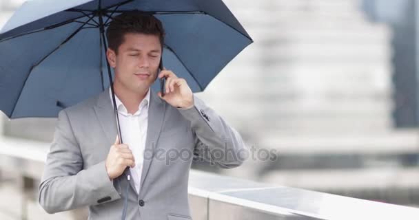 Businessman in city holding umbrella talking on smartphone - Video