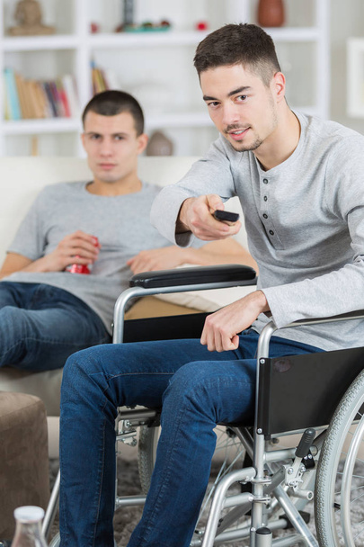 young handicapped man watching television with friend - Фото, изображение