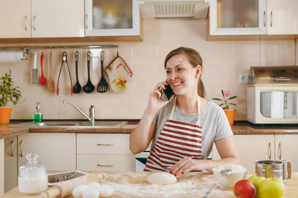 Una joven hermosa mujer feliz sentada en una mesa con harina e ir a preparar un pastel de Navidad en la cocina. Cocinar en casa. Preparar alimentos
. - Foto, imagen