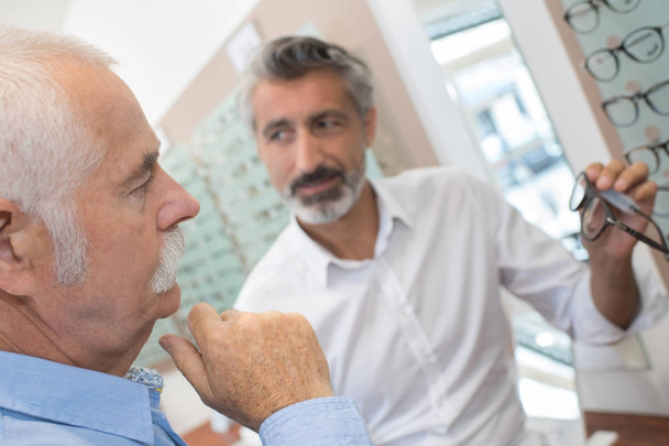 male optician consulting senior customer near display - Фото, изображение