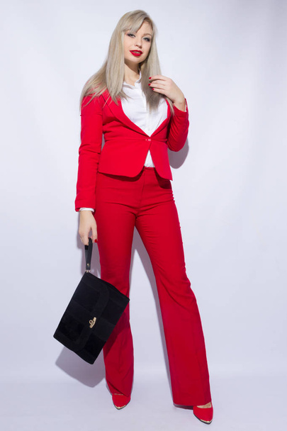 Portrait of a beautiful young blond woman with long hair in a red suit. She holds a big black clutch in her hand - Foto, imagen