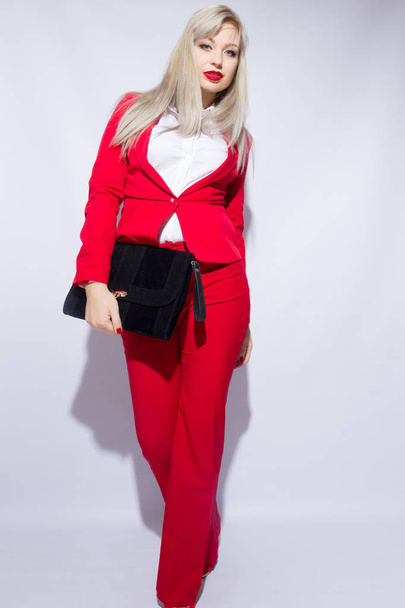 Portrait of a beautiful young blond woman with long hair in a red suit. She holds a big black clutch in her hand - Fotoğraf, Görsel