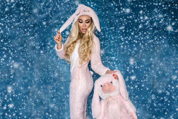 Mooie sexy blonde vrouw die het dragen van een pyjama, een bunny kostuum, lacht gelukkig. Fotomodel op de achtergrond van een winter. - Foto, afbeelding