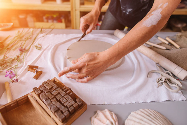 Master ceramist rubs a plate of baked clay. A creative workshop. - Zdjęcie, obraz