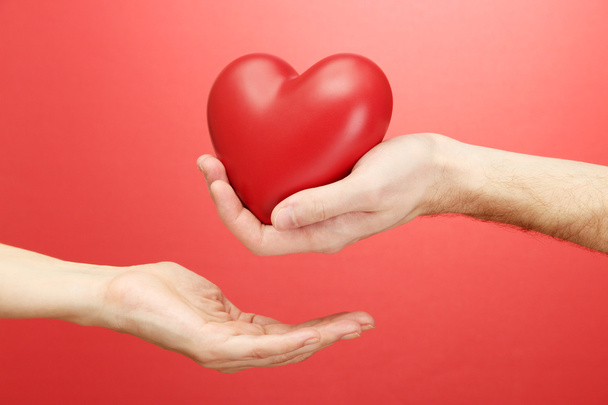Corazón rojo en manos de hombre y mujer, sobre fondo rojo
 - Foto, imagen