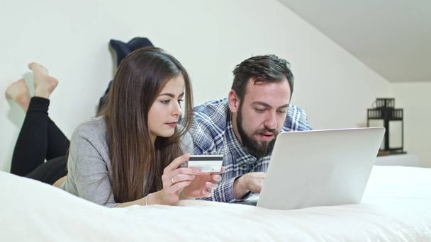 glückliches Paar mit einem Laptop, der zu Hause auf dem Bett liegt - Foto, Bild