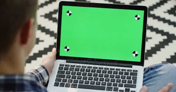 Close up of the view over shoulder on the man sitting with a laptop on his knees and typing on it. Green screen. Chroma key. Tracking motion. Patterned carpet background - Filmati, video