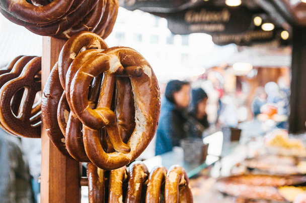 Traditional pretzels called Brezel hang on the stand against the background of a blurred street market and people on holiday. - Photo, Image