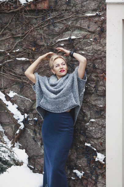 Cute woman in gray sweater stands against stone wall - Foto, afbeelding