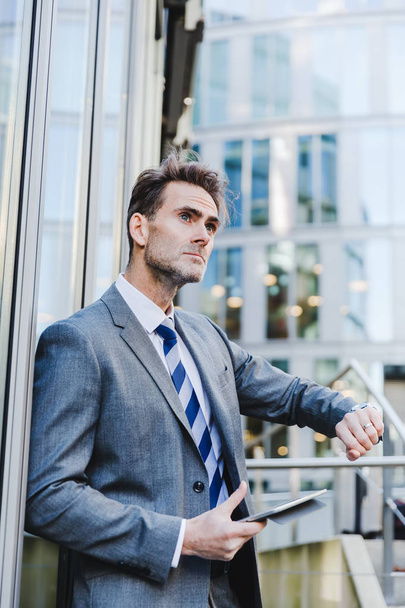 businessman leans against an office building and watches the time - Photo, image