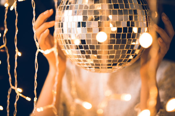 Close-up shot van vrouw aanraken disco bal met mooie slingers rond - Foto, afbeelding