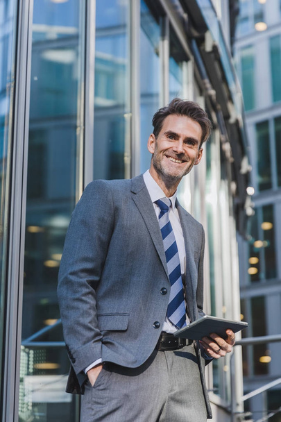 businessman stands in front of an office building with a tablet - Foto, Imagem