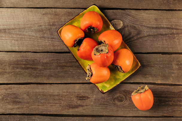 top view of persimmons on yellow bowl on striped wooden table - Photo, Image