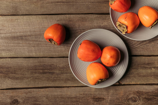 top view of persimmons on plates on wooden table - Foto, Imagem