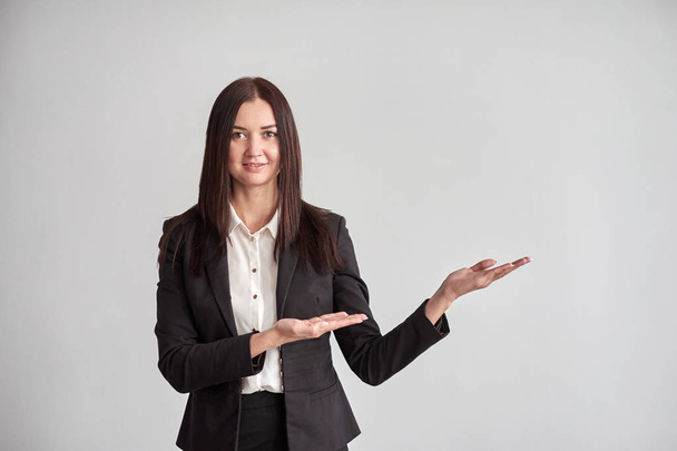 Smiling young businesswoman, showing something, some product or blank copyspace area for advertise slogan or text message, on a gray wall in the office - Foto, Imagem